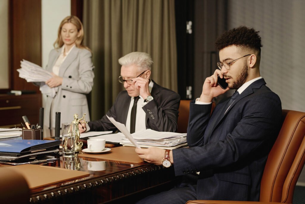 Young middle eastern lawyer having business call on cellphone, his colleagues doing paperwork nearby