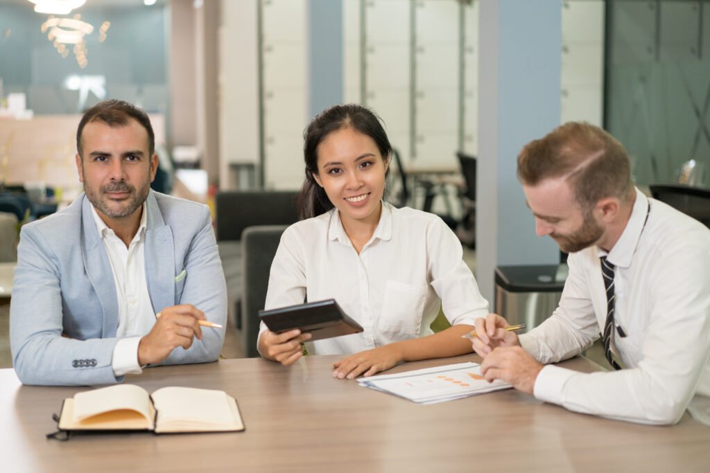 Positive business people working with diagram in office. Multiethnic businesspeople looking at camera and sitting with modern blurred interior in background. Business analysis concept.
